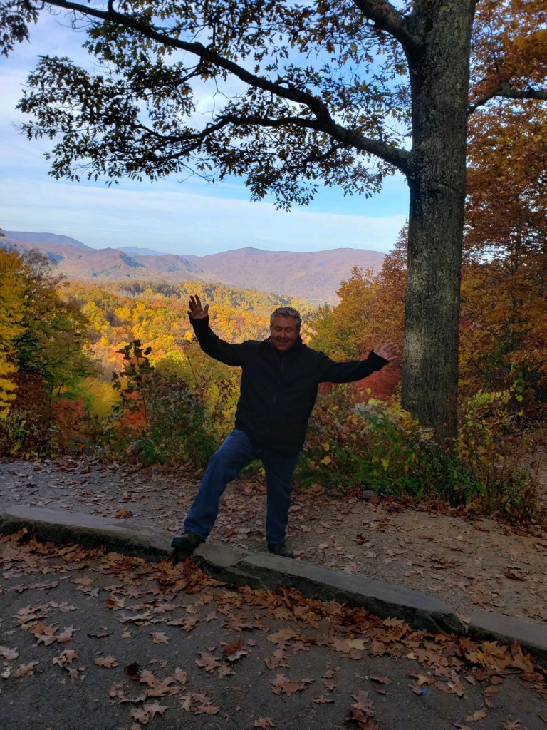 a man standing on a dirt path with Smoky Mountains in the background