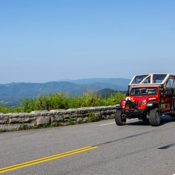 Red open-top jeep on mountain road with scenic view.