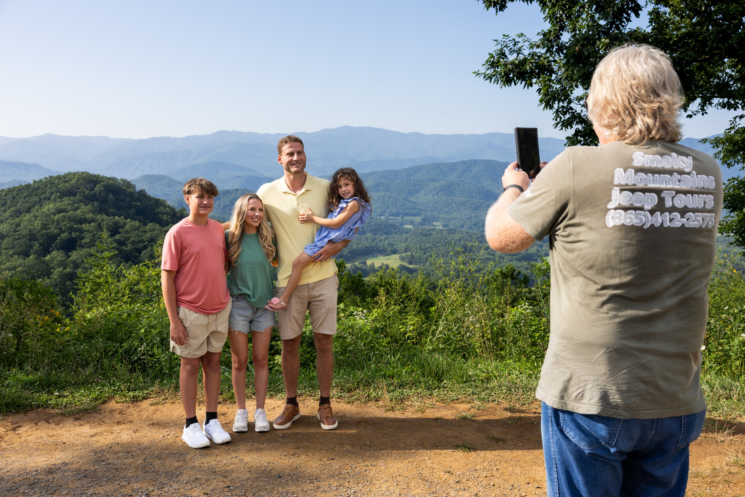 Family of four smiling in front of scenic mountain view taking a Smoky Mountains Jeep Tour.