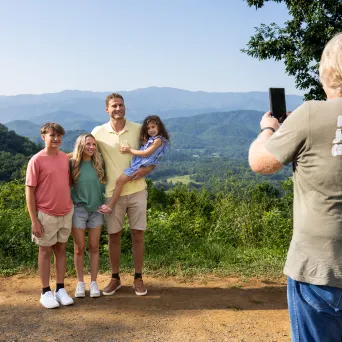 Person taking photo of four people with mountains in the background.