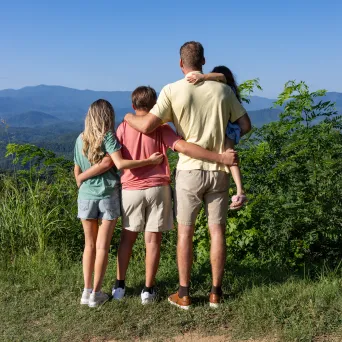 Four people from behind, embracing, overlooking a mountain landscape.