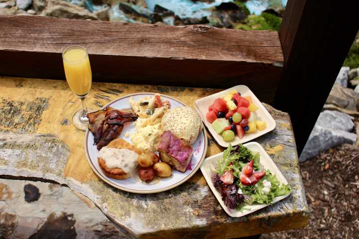 Plate of breakfast food, salad, fruit, and a glass of orange juice on a rustic table.