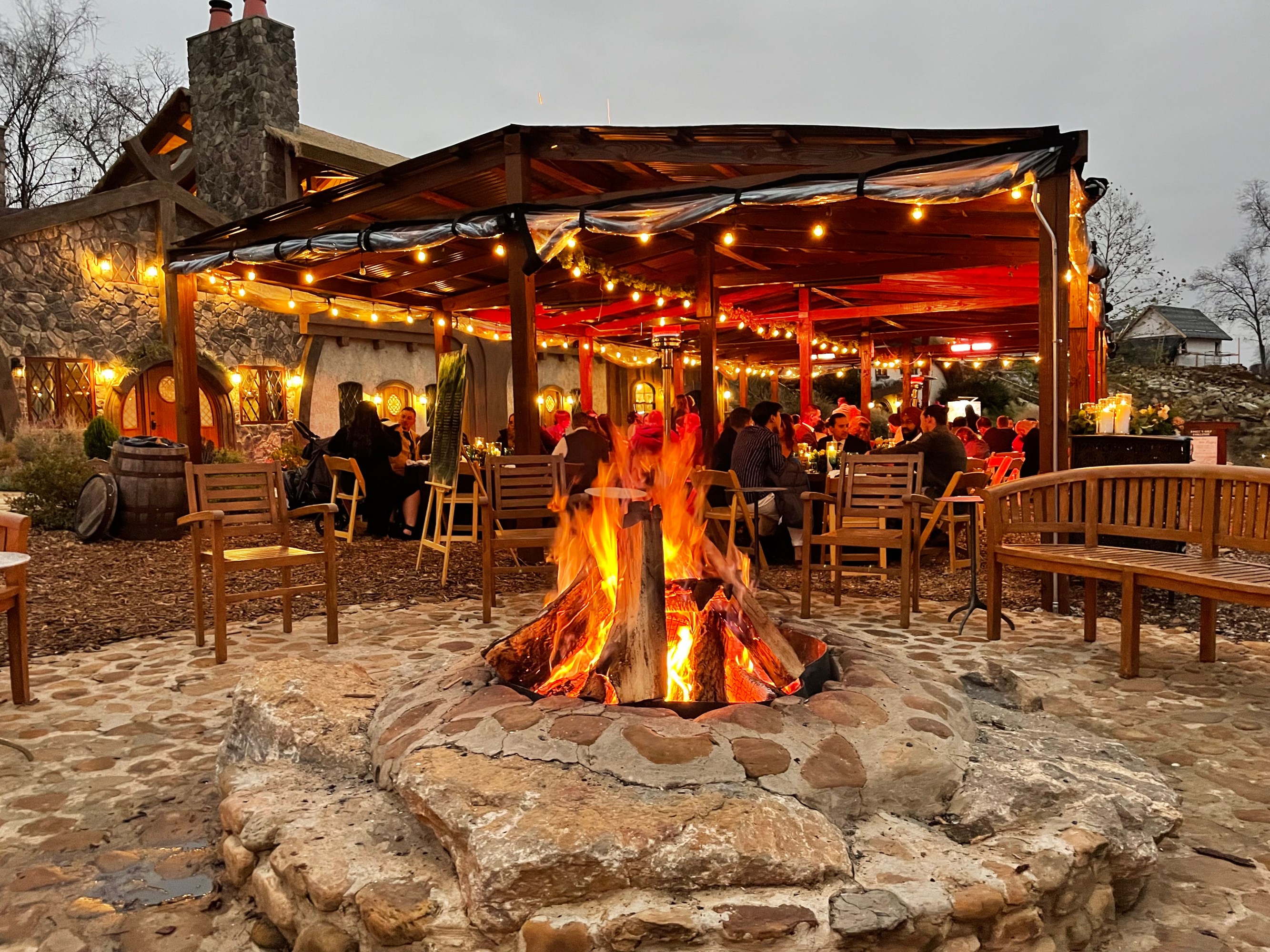 Outdoor seating with a stone fire pit, wooden pergola, and string lights at dusk. Ancient Lore Village Scenic Tour and Lunch with Smoky Mountains Jeep Tours.